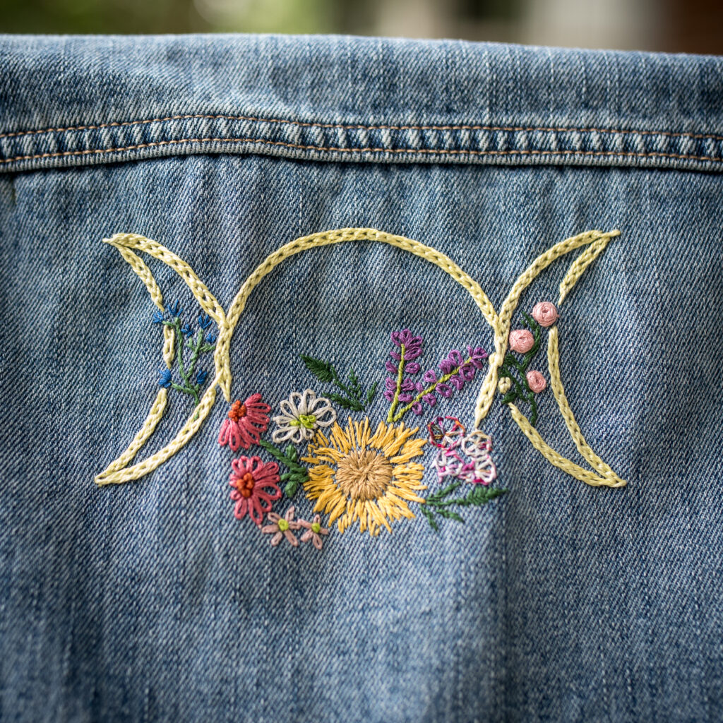 a denim jacket back with triple moon and flowers embroidered on it