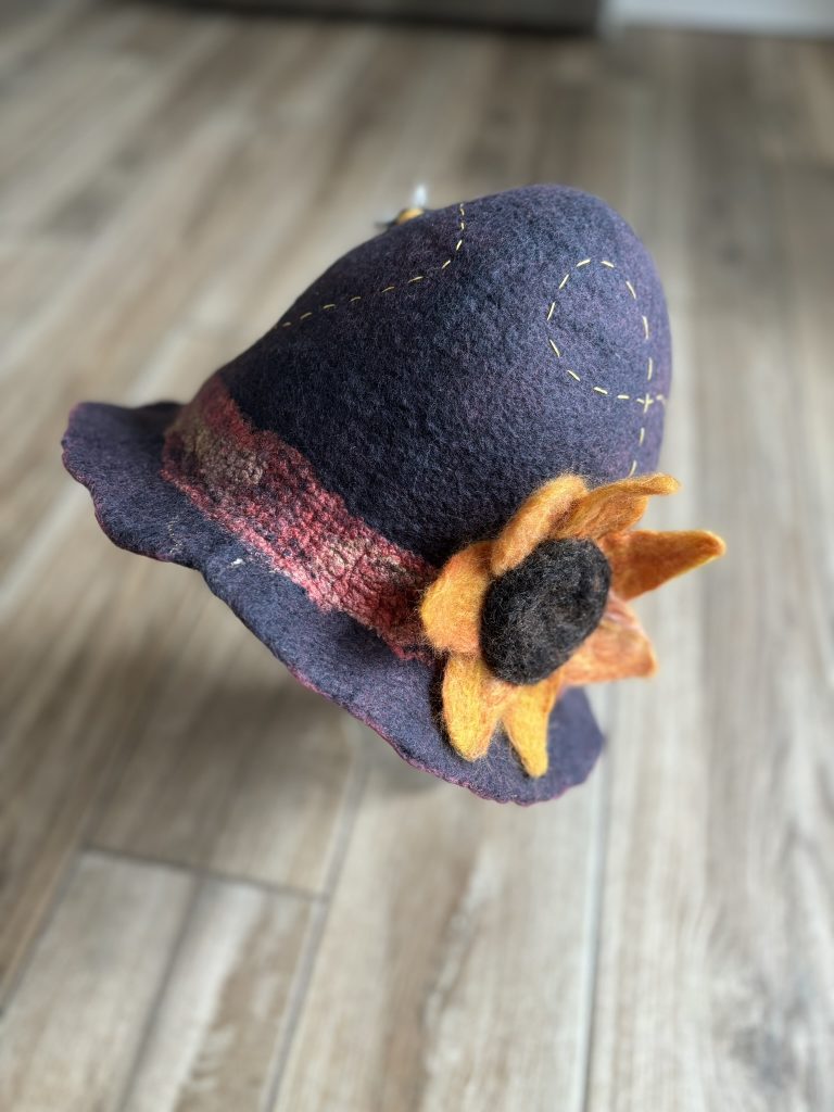 A grey-purple cloche hat with a yellow felted sunflower on the band