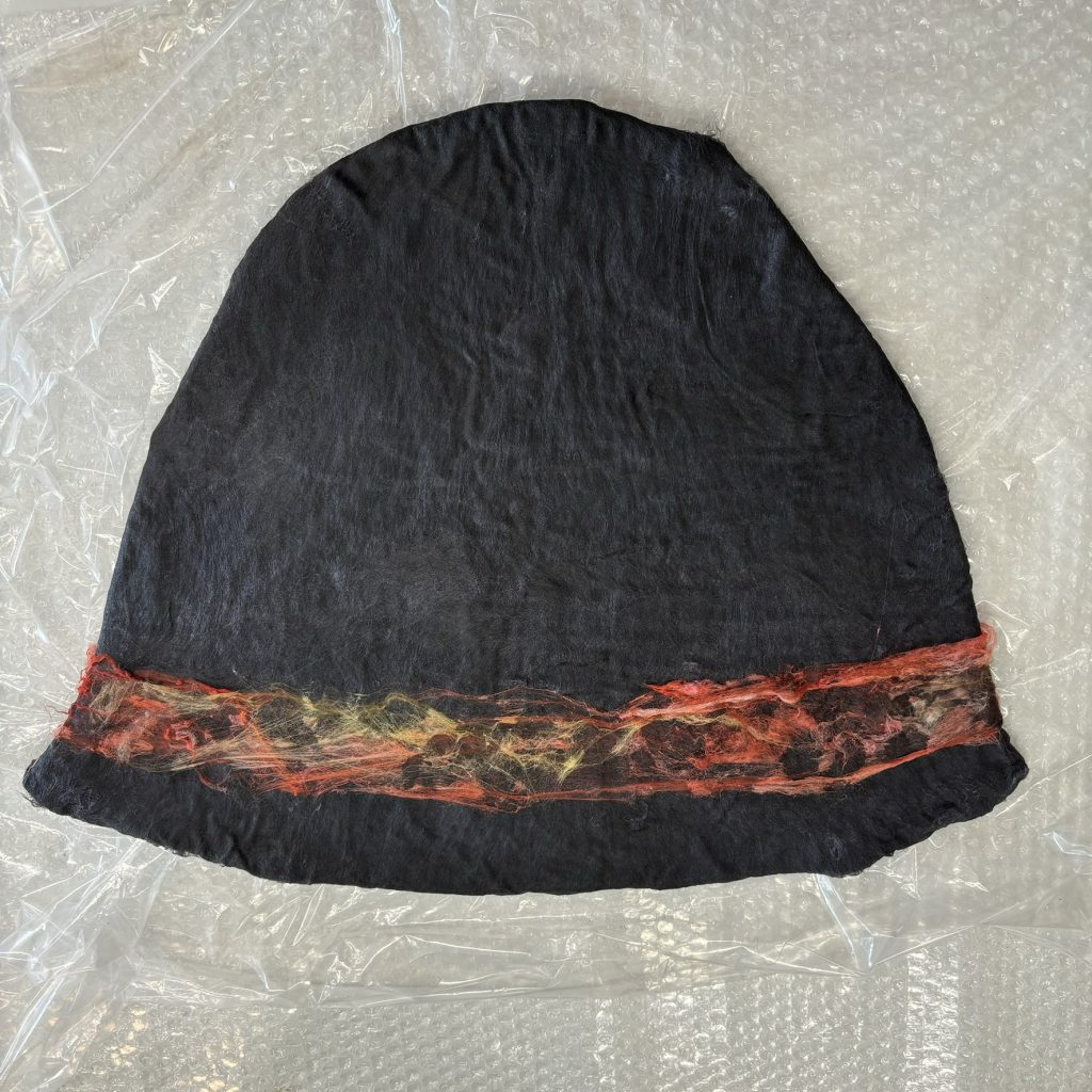 a flat hat shape in wet wool, beginning to be felted, with silk embellishment