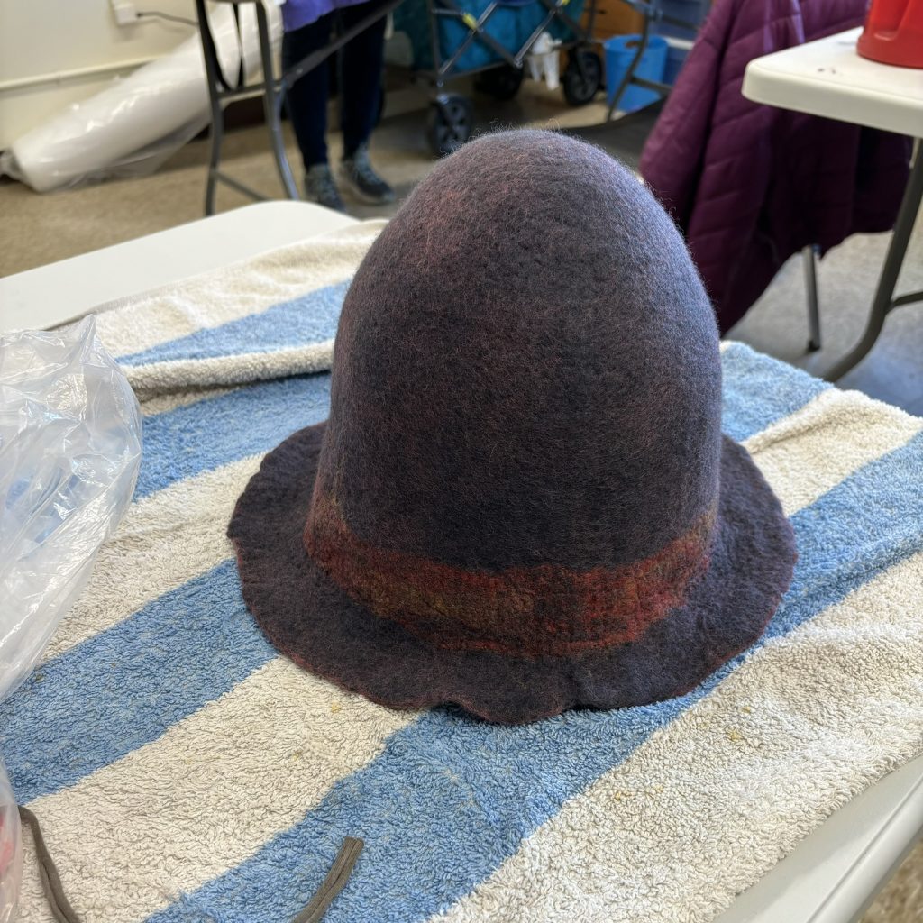 A tall newly made grey cloche wool hat. The coral from the inside shows through the wool a bit, and there is coral and yellow silk embellishment.