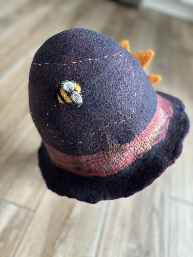 A grey cloche hat with a felted bee buzzing around it
