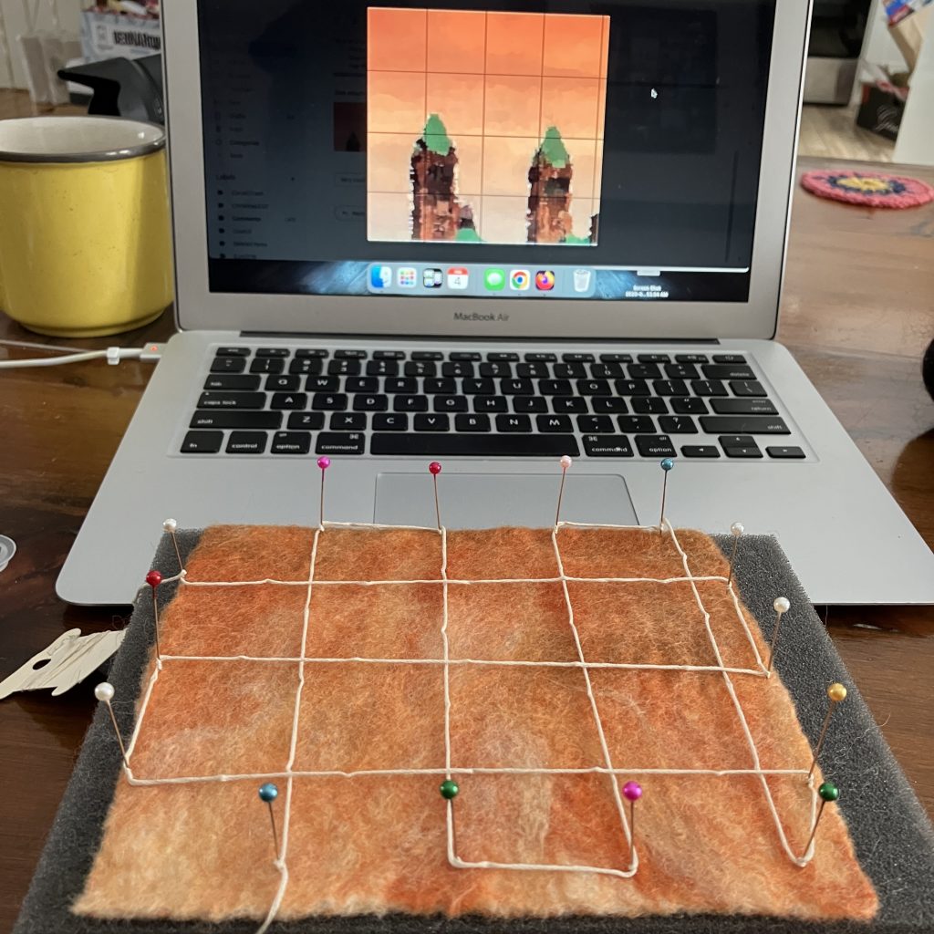 An image on the laptop screen in background with a felt square that has beed divided into grids in the foreground