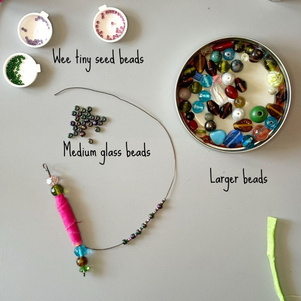 Image of workspace with three types of beads (seed, medium and larger mixed) and a boho fabric bead in progress