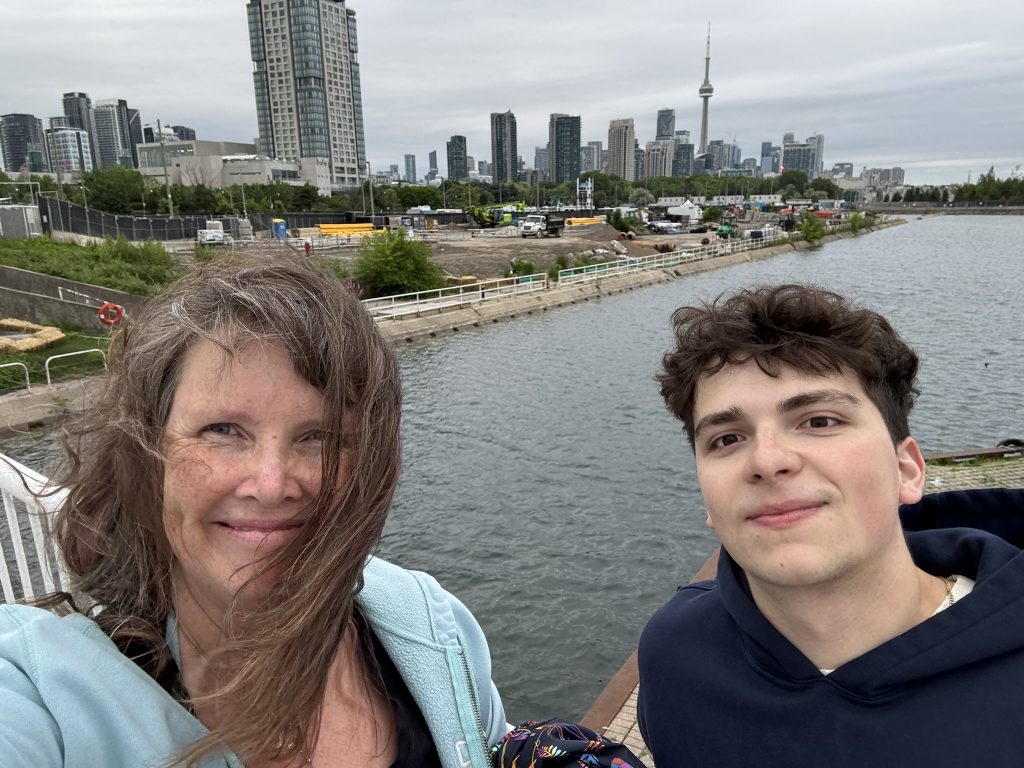 Dani and Simon in the foreground of a selfie taken with the Toronto skyline and waterfront in the background
