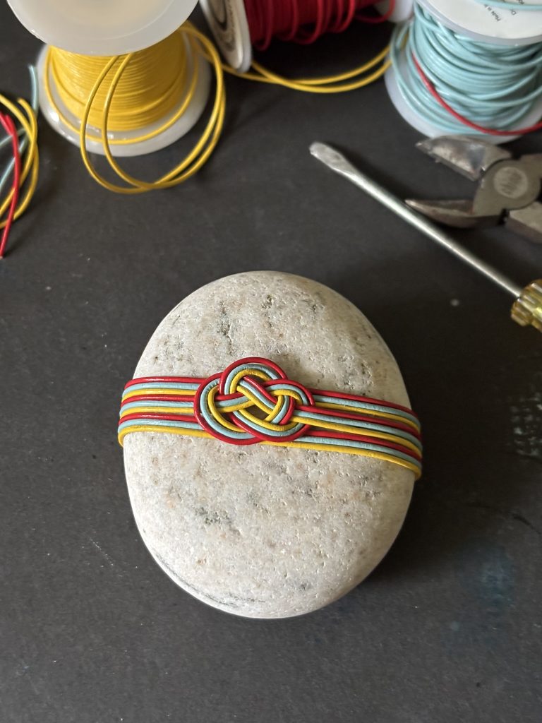 A white rock wrap with three colourful strands in an awabi or abalone knot