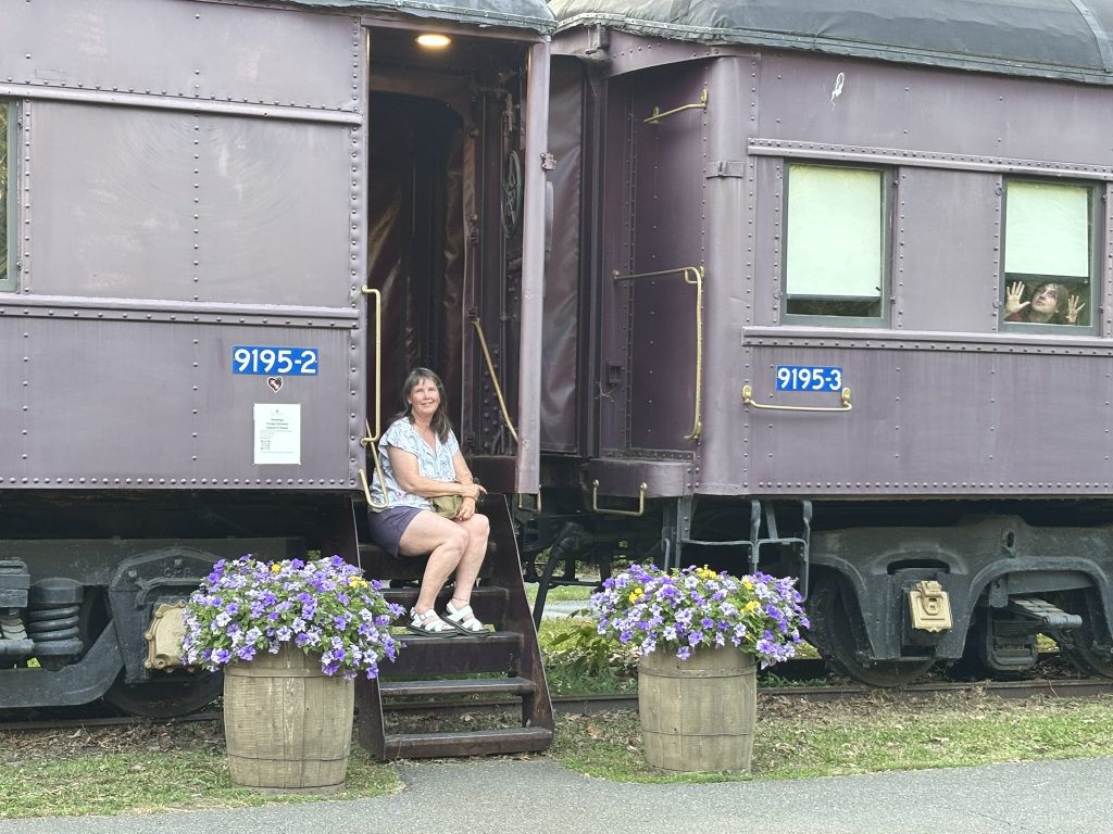 Dani sitting on the rail car at the Adventure on Rails hotel while Tristan mugs in the window