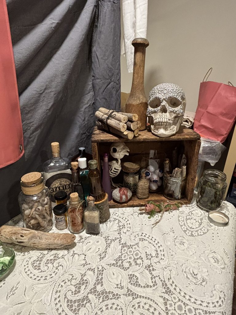 alchemist-themed tarot reading booth for a pop up renaissance fair including lace table cloth, bedazzled skull, bottles, sticks and bones